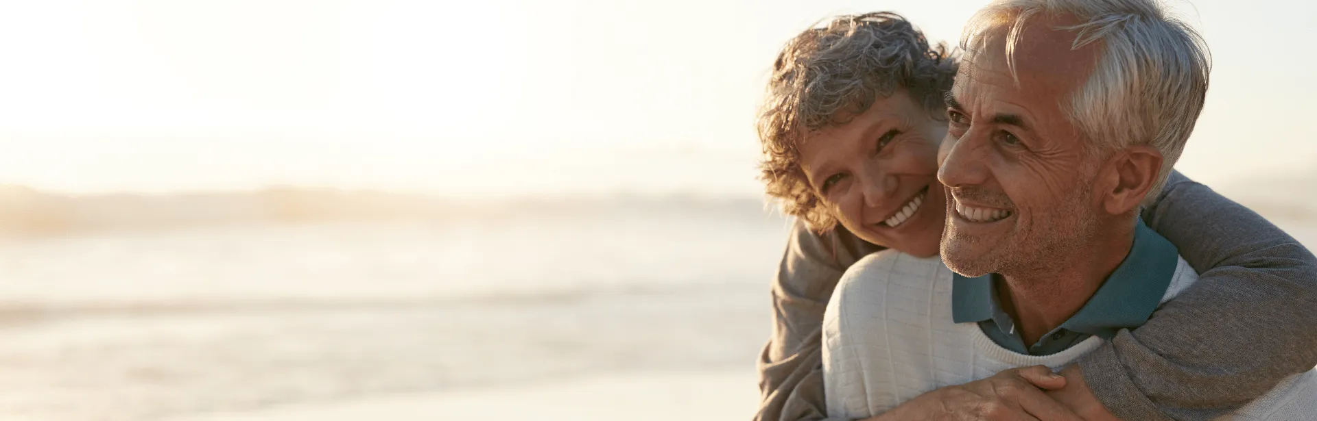 A senior couple embracing each other on a beach with waves in the background.